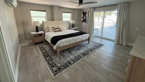 Un dormitorio con cama, mesitas de noche, ventilador de techo y vistas al exterior.
