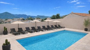 Ein Pool mit Liegestühlen und Sonnenschirmen, umgeben von einer niedrigen Mauer und Topfpflanzen.