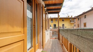 Un balcón de madera con un tapete verde, una puerta de madera y vistas a edificios cercanos.