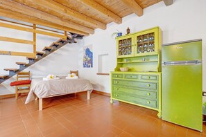 Un dormitorio con una cama, un aparador verde, un refrigerador, una escalera de madera y un cuadro en la pared.