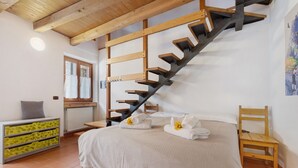 Un dormitorio con una cama, una silla de madera, un aparador, una escalera de madera y un ventanal.