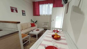 En matplats med ett bord för två personer, en soffa och ett köksområde med en bänkskiva.