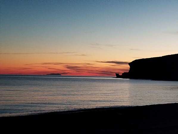 Ein Küsten-Sonnenuntergang mit der Silhouette einer Klippe und ruhiger See.