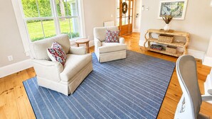 A living room with two sofas, a coffee table, and a rug. There is a door leading to a hallway. - Falmouth Foreside Cottage Escape - Luxe Kitchen + Walk to the Water! (Falmouth)