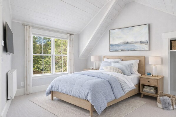 A bedroom with a sloped ceiling, a bed with a headboard, two bedside tables with lamps, a painting above the bed, and a window with curtains. - Falmouth Foreside Cottage Escape - Luxe Kitchen + Walk to the Water! (Falmouth)