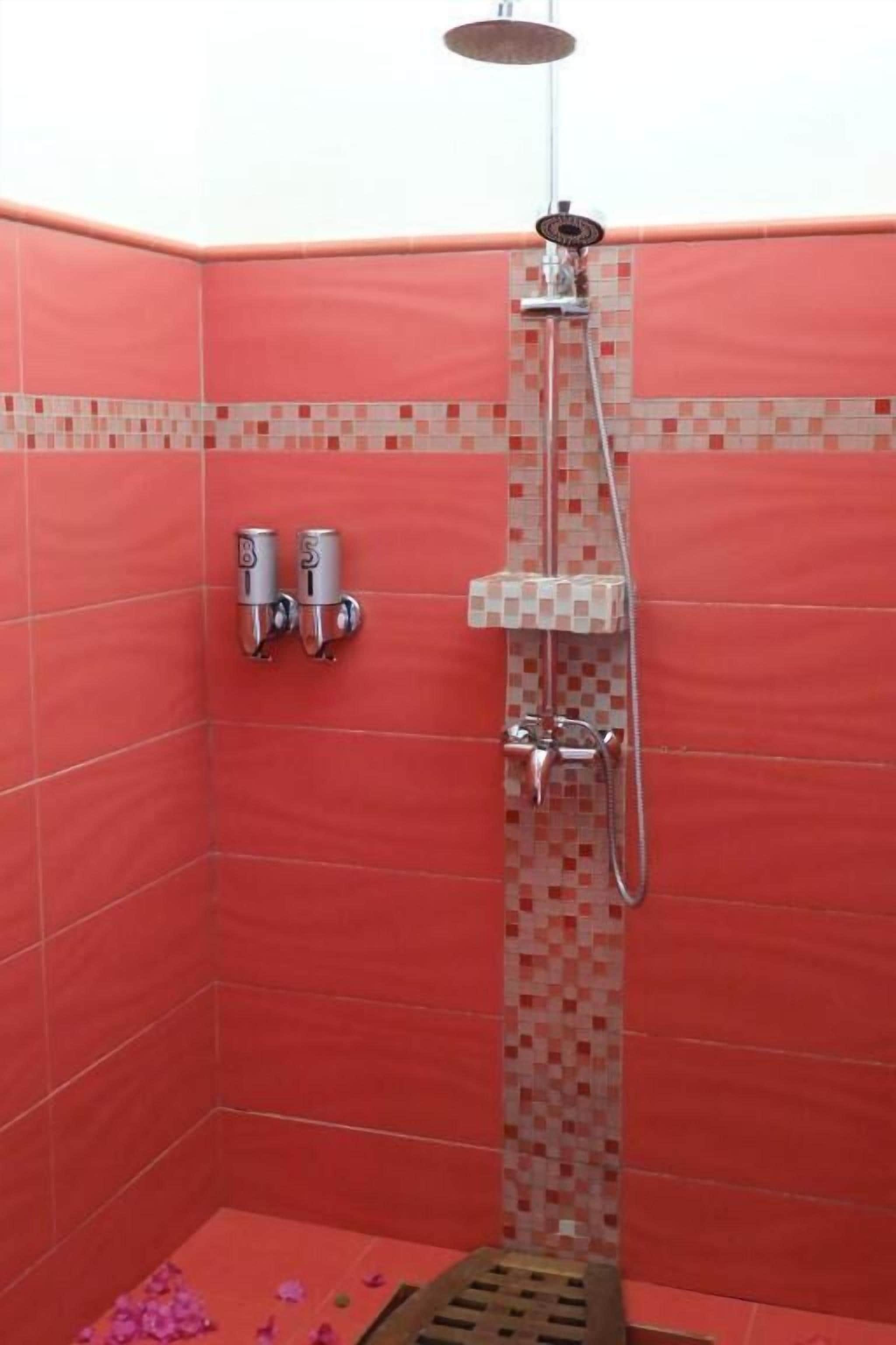 A shower with a handheld showerhead, a wall-mounted faucet, and a tiled floor.