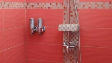 A shower with a handheld showerhead, a wall-mounted faucet, and a tiled floor.