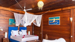 Une chambre à coucher comprenant un lit, un ventilateur de plafond, une table de chevet, une commode, une chaise et un tableau accroché au mur.