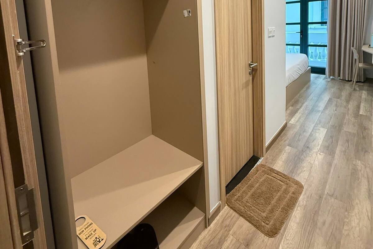 A room with a large wardrobe, a bed, a small desk, and a window with curtains.