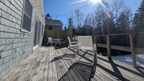 En træterrasse med udendørs møbler, et træhegn og et hus i baggrunden.