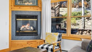 A cozy room with a fireplace, a window with a view of a wooden deck, and a checkered chair.