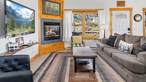 A cozy living room with a fireplace, a television, a sofa, and a view of the outdoors.