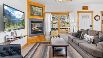A cozy living room with a fireplace, a television, a sofa, and a view of the outdoors.