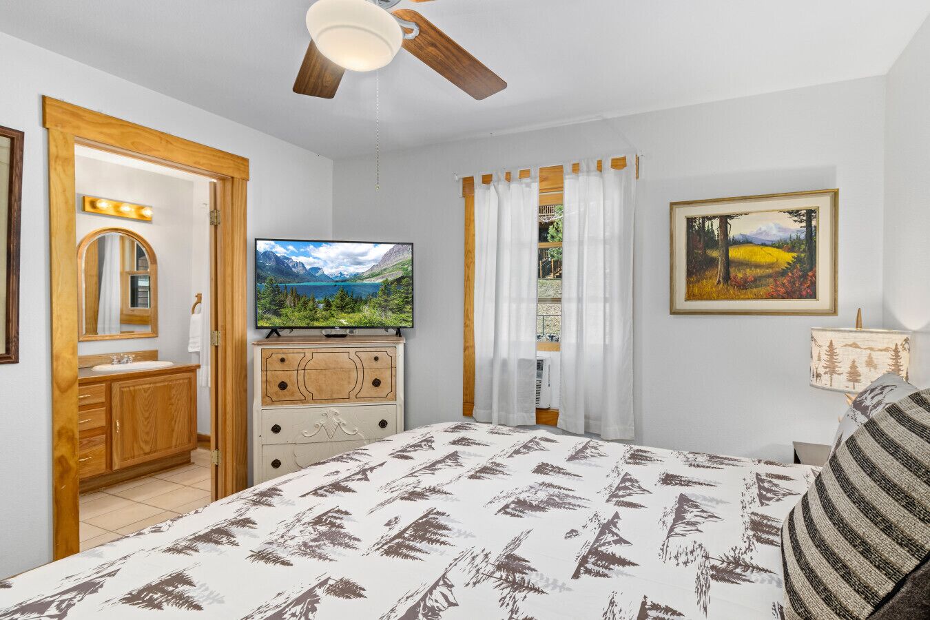 A bedroom with a bed, a television, a dresser, a mirror, a window with curtains, and a painting on the wall.