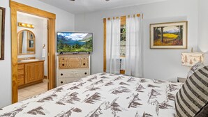 A bedroom with a bed, a television, a dresser, a mirror, a window with curtains, and a painting on the wall.