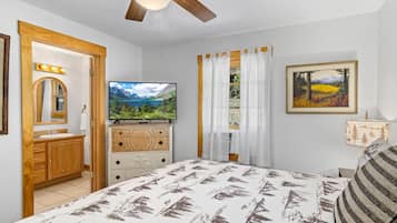 A bedroom with a bed, a television, a dresser, a mirror, a window with curtains, and a painting on the wall.