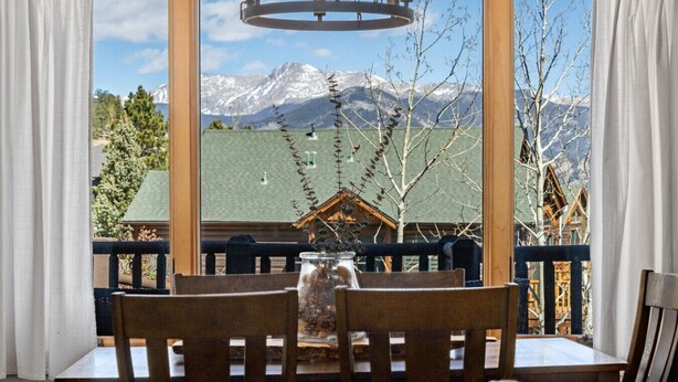 A dining area with a table and chairs, a chandelier, and a view of snow-capped mountains through large windows.