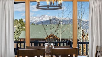 A dining area with a table and chairs, a chandelier, and a view of snow-capped mountains through large windows.