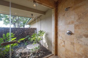 Eine moderne Dusche mit Steinsturz, Glastür und Blick auf einen Garten mit Pflanzen und einer Steinwand.