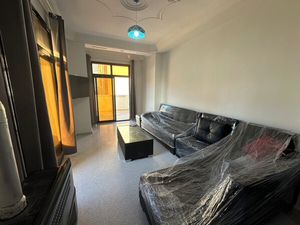 Una sala de estar con sofá, mesa de centro, televisor y puerta corrediza de vidrio que da a un balcón.