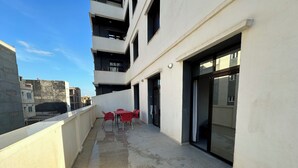 Un balcón con una mesa y sillas, un ventanal de vidrio y vista panorámica de la ciudad.