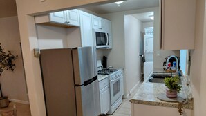 Una cocina con armarios blancos, un refrigerador de acero inoxidable, un microondas, una estufa y un lavaplatos.