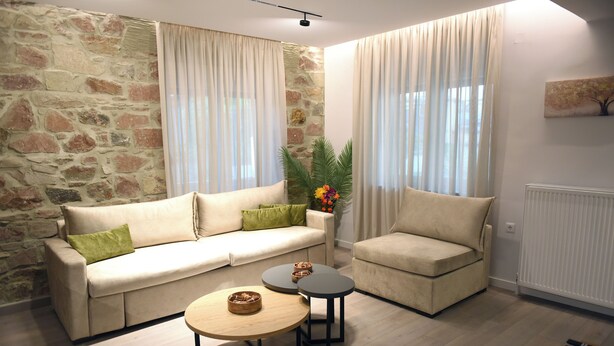 A living room with a stone wall, a sofa, a chair, two small tables, and a radiator. - CozyFlat 88m2 very spacious for long stays, fully equipped, with private parking (Mitilini)