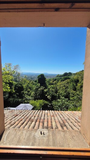 A terrace with a tiled roof, a view of a green landscape, and a clear blue sky.