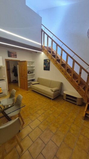 A spacious living area with a wooden staircase, a beige sofa, and a glass dining table.