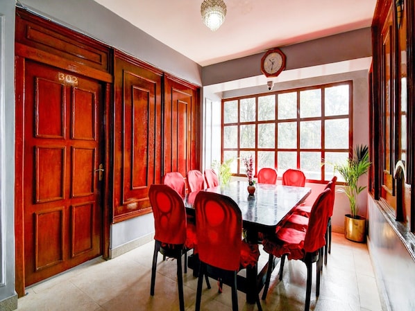 A dining area with a large wooden door marked '302', a long table with red chairs, and a clock on the wall.