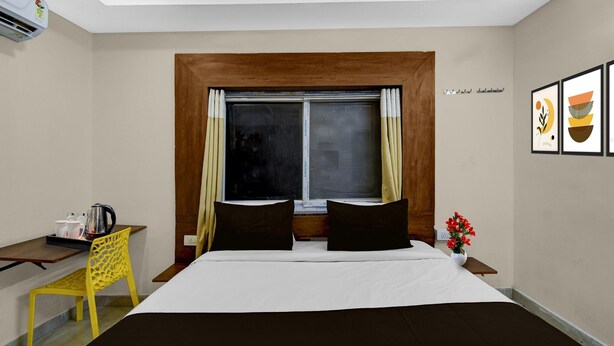 Habitación de hotel con cama, escritorio con cafetera, silla, ventana con cortinas y una pared decorada con obras enmarcadas.