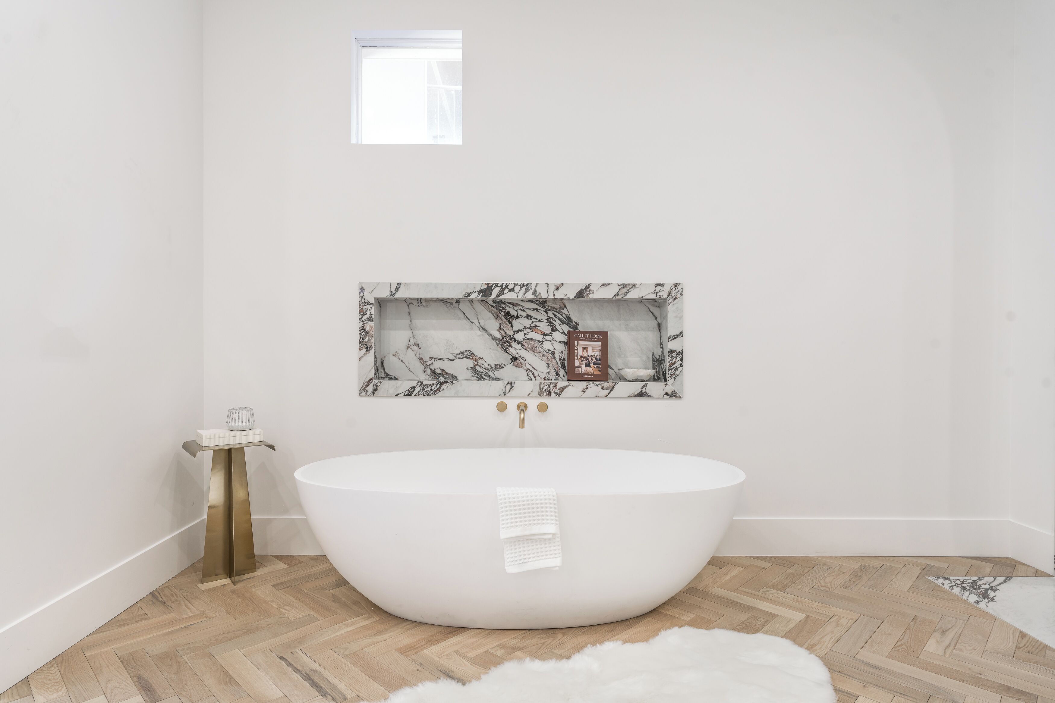 A modern bathroom with a freestanding bathtub, a marble-framed artwork, and a small side table with a cup.
