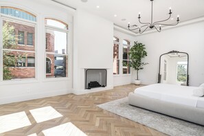 Un dormitorio amplio con ventanas grandes, chimenea, cama y candelabro.