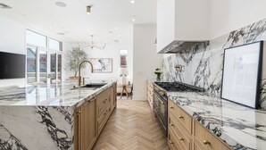Cocina moderna con encimeras de mármol, armarios de madera y suelo en espiga.