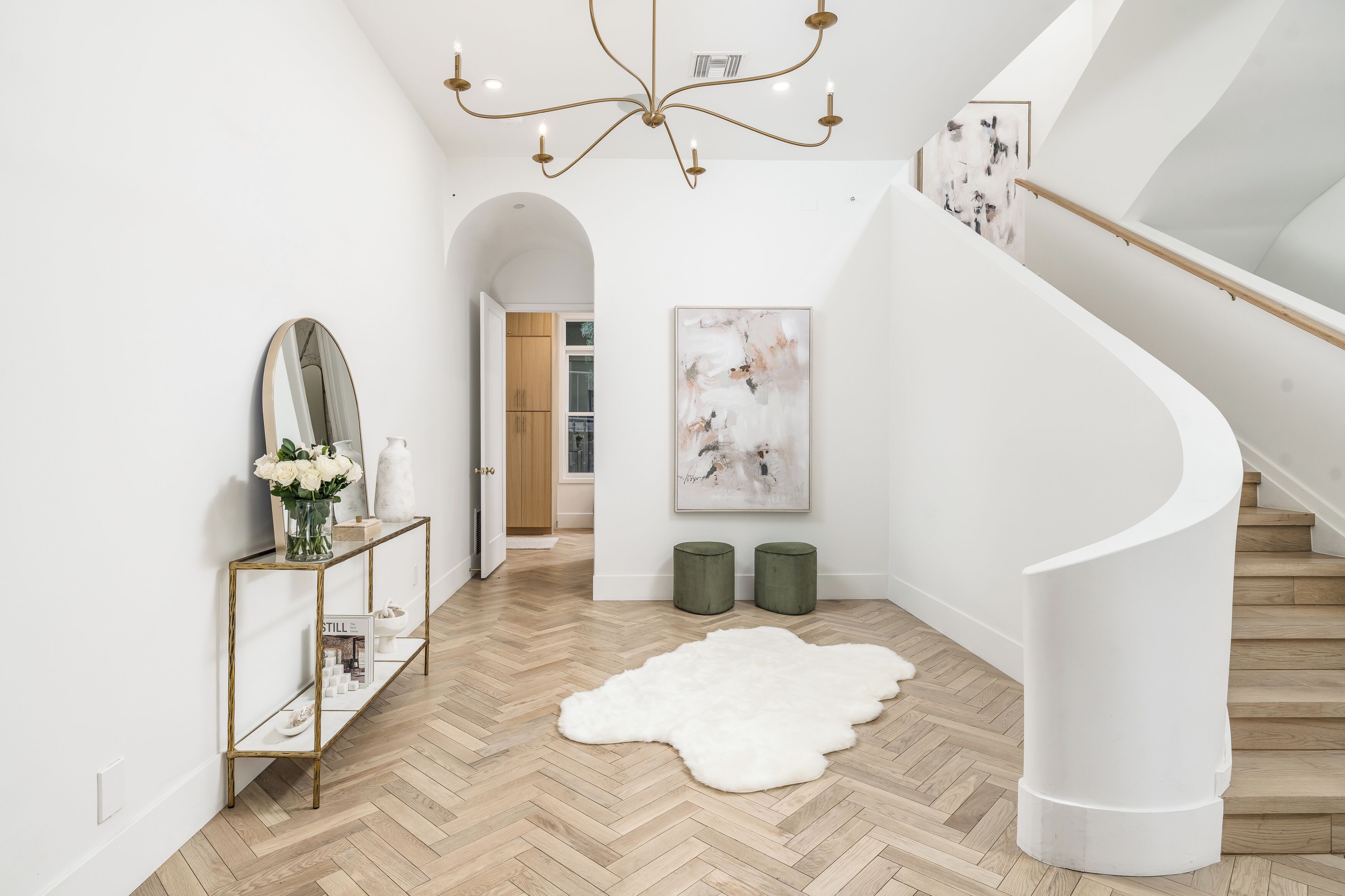 A modern interior with a herringbone wooden floor, a white console table with a mirror, a white shag rug, and a spiral staircase.