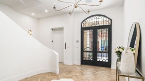 Un interior moderno con piso de madera en patrón de espiga, una escalera blanca, una puerta negra con reja de hierro forjado y un manto blanco de piel.
