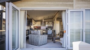 Eine offene Schiebetür führt in einen Wohnbereich mit einer Couch, einem Tisch und einer Küche im Hintergrund.