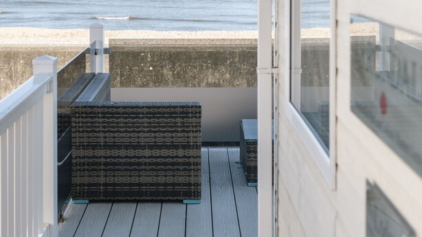 Ein Balkon mit Blick auf das Meer, eine Korbsitzbank und eine Tür zum Innenbereich.
