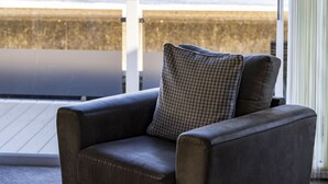 Ein dunkelbraunes Sofa mit einem karierten Kissen in einem Raum mit einem großen Fenster mit Blick auf ein Gew ässer und ein entferntes Land.