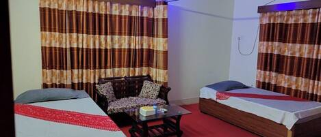 A room with two beds, a sofa, a coffee table, and curtains.