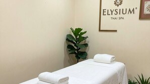 Une salle de spa équipée d’une table de massage, de serviettes, d’une plante en pot et d’une enseigne indiquant « Elysium Thai Spa ».