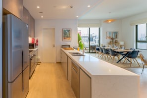 A modern kitchen with stainless steel appliances, a dining area with a large table and chairs, and a view of the city through large windows. - Le Ciel - 2BR Beachfront with Amazing City and Burj Khalifa View (Port De La Mer)