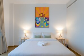 Ein Hotelzimmer mit Bett, zwei Nachttischlampen, einem Wandbild und einem Fenster mit Vorhängen.