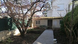 A paved pathway leading to a building with a door and windows, surrounded by trees and a fence. - Charming bungalow with garden in a quiet neighborhood (Montreuil)