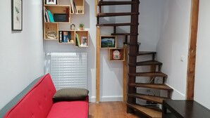 A room with a red sofa, wooden shelves, a radiator, and a wooden staircase. - Charming bungalow with garden in a quiet neighborhood (Montreuil)