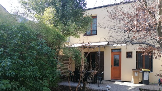 A building with a paved entrance, a wooden door, and a window with a metal grill. - Charming bungalow with garden in a quiet neighborhood (Montreuil)