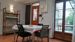 A dining area with a table and chairs, a bookshelf, a door with a view, and a thermostat on the wall. - Charming bungalow with garden in a quiet neighborhood (Montreuil)