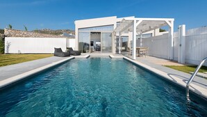 Un espace piscine extérieur moderne, offrant une vue dégagée sur la piscine, un coin salon couvert et un mur de pierre en arrière-plan.