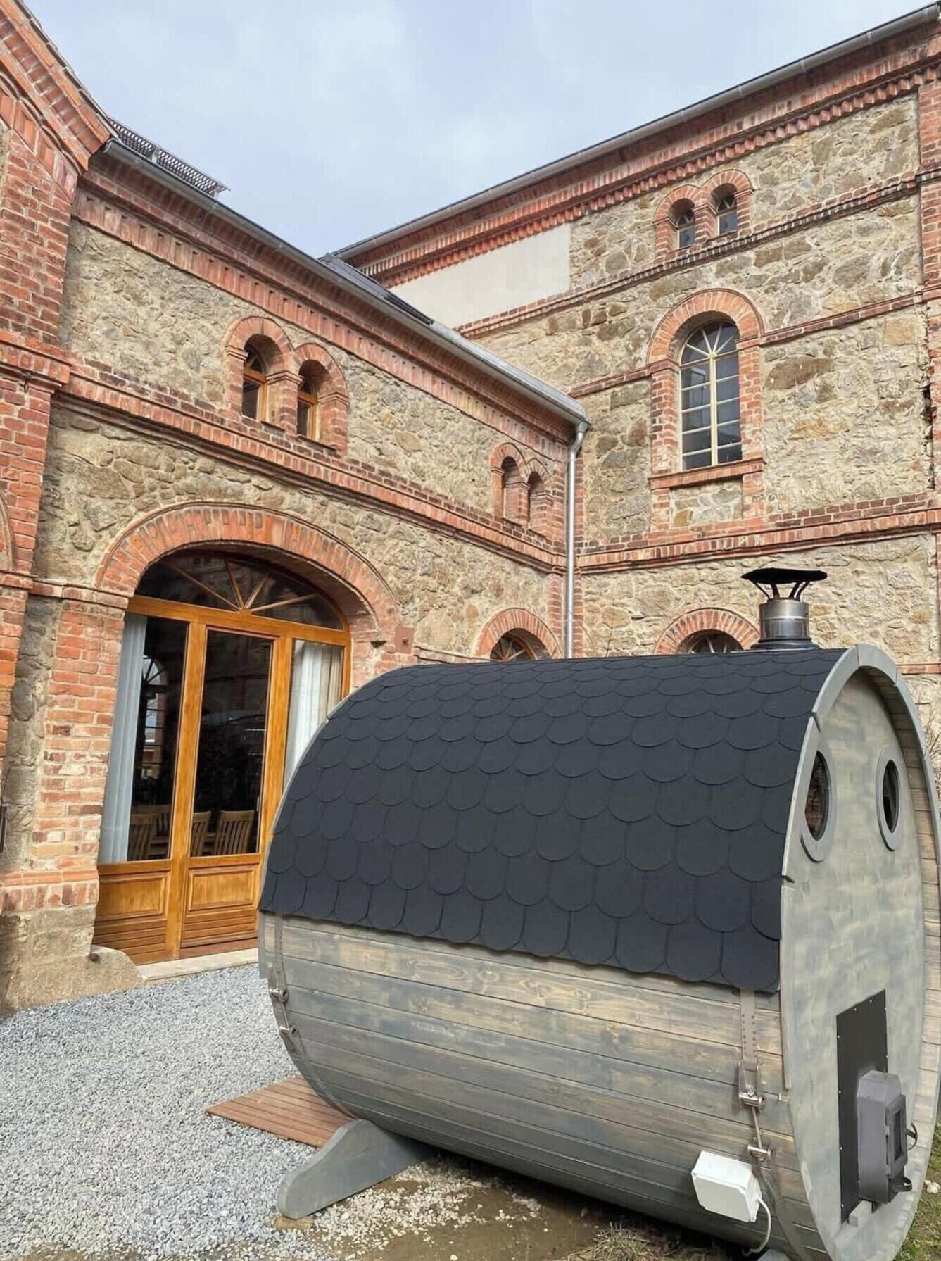Um edifício de pedra com janelas em arco e uma grande estrutura cilíndrica em frente.