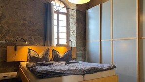 A modern bedroom with a stone wall, a large window, a bed with a wooden headboard, and a sliding door. - A Two-storey Home With Terrace and Fireplace - Last Minute (Grossharthau)